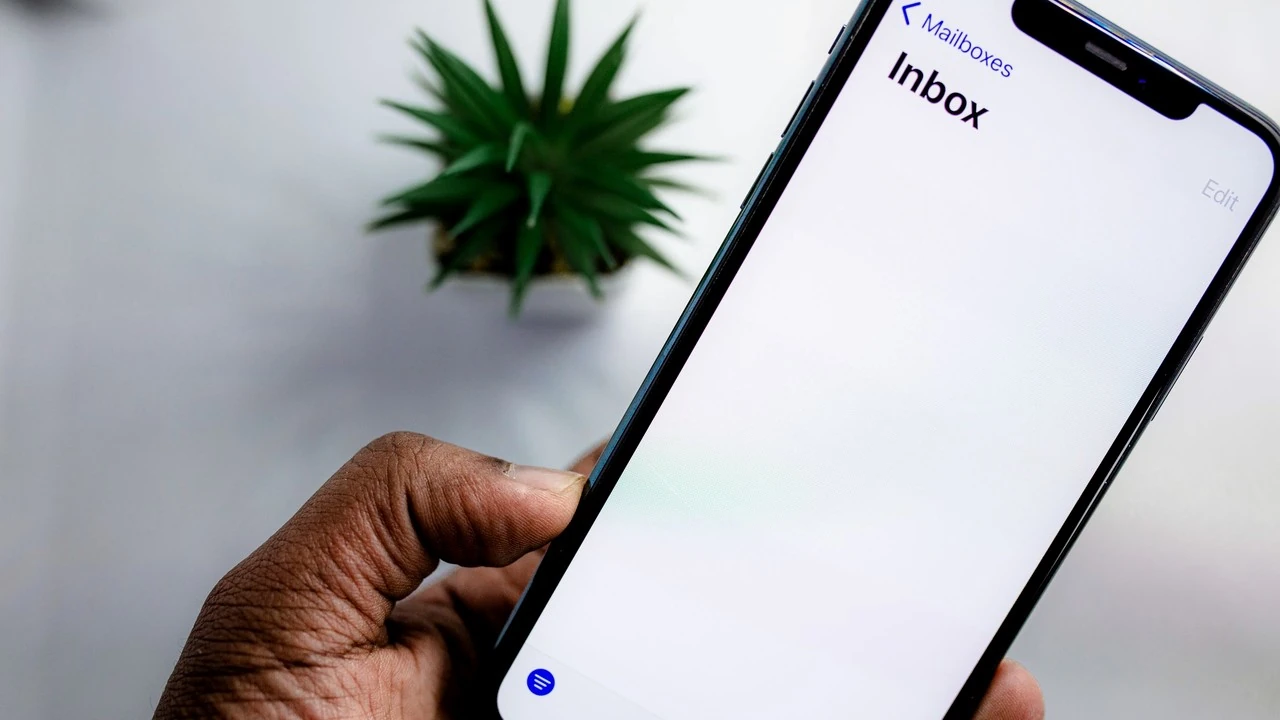 A hand holding a smartphone with the mail inbox open on its screen